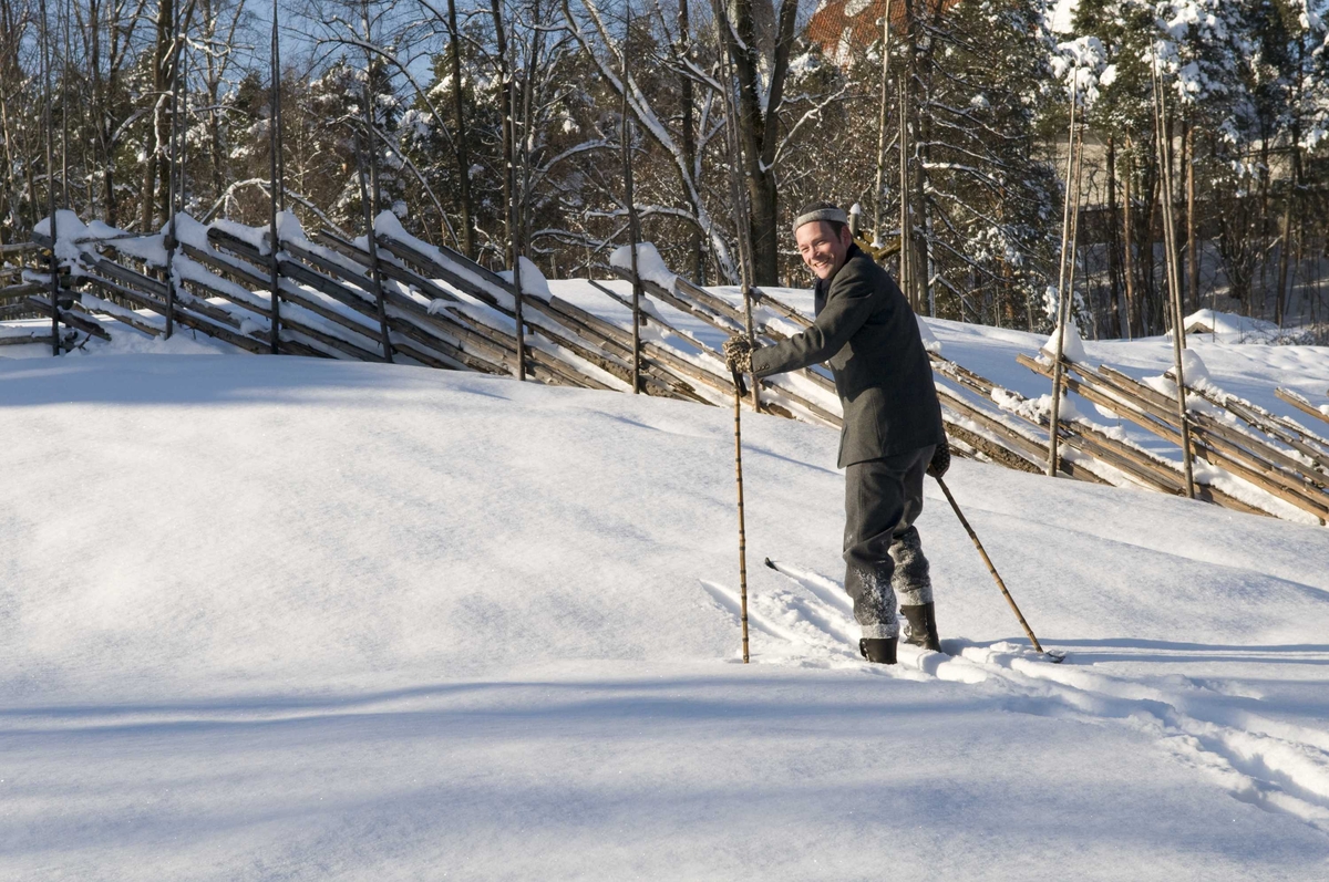 En serie med bilder av utkledd mann i klær anno 1870-1900 som går på ski på jordet bak festplassen.
Illustrasjonsfotografier.