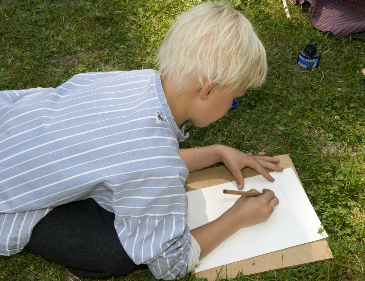 Ferieskolen uke 27, 2009.
Undervisning foregår utendørs, barna lærer å skrive med blekk.
