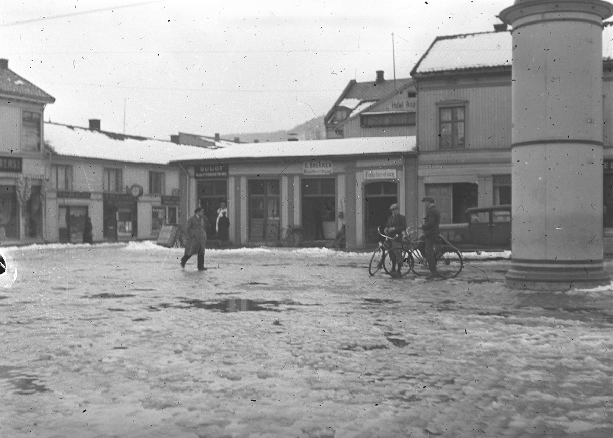 Gatebilde. Menn på sykler på torget.