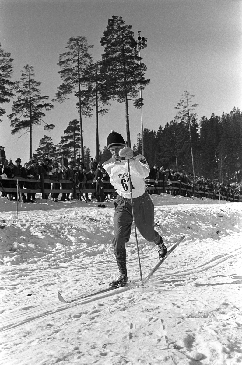 Skiløper med startnummer 61 i Holmenkollen. Publikum langs løypa.   Holmenkollrennene 1963.