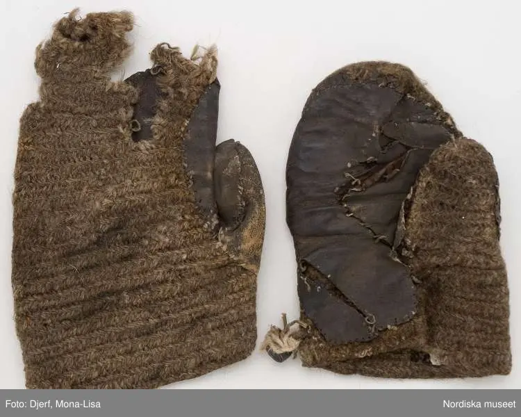 1 par tumvantar för maan av  gråbrunt ullgarn i nålbindning.  På handens insida  skodda med brunt skinn påsytt med grått lingarn. På högervantens handled en knapp av hoprullad skinnremsa  fäst med en skinnrem. Motsvarande ögla bör ha funnits på den andra vanten som dock är så pass trasig att inget finns kvar vid handleden.
/Berit Eldvik 2013-03-18