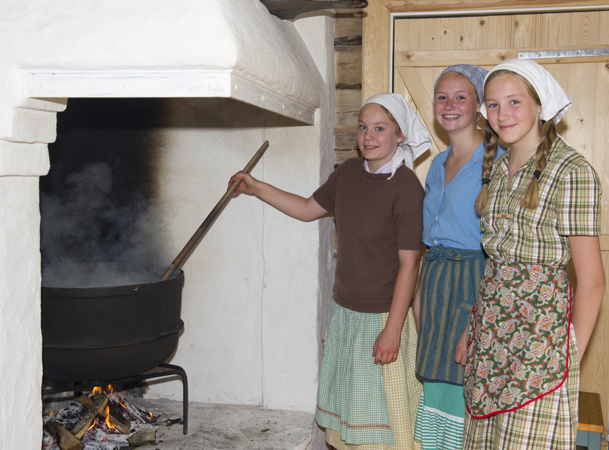 Trønderskolen anno 1959. Norsk Folkemuseums sommertilbud til ungdom. Deltakerne prøver seg på praktiske arbeidsoppgaver som det var vanlig at ungdom deltok på for 50 år siden. Trøndelagstunet på Norsk Folkemuseum. Jenter som yster eller koker i kjele i grua.