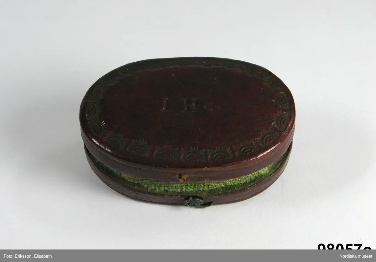 Manschettknappar, två par, miniatyrer. 1700-tals mitt.  Silver, glas.
Saknar stämplar. På varje knapp ett ovalt porträtt i miniatyr i silverinfattning, baksidan räfflad, knapparna förenade två och två, på den ena föreningslänken. ”I H” i genombrutit arbete, den andra föreningslänken senare ersättning. Manschettknapparna hölls i ett rött marokäng (getskinn) etui.
(katalogiseringen gäller a-c)