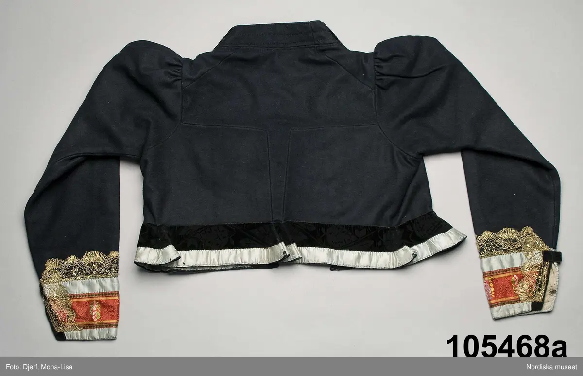 Kvinnotröja, från början en brudtröja av svart  kläde, 2 framstycken/sidstycken med infällda skörtkilar i sidorna, ett ryggstycke med mycket smal mittdel med rätvinkliga sömmar mot sidorna. Mittdelen bildar nedtill ett skört, små tränsade skörtstopp av blått silke. Isydd rak ärm med en söm med 8 cm ärmsprund knäppt med hake och hyska, rynkad vidd på ärmkullen. Framkanterna svängda, i halsen uppstående rak ståndkrage. Kantad runtom med, ytterst ett ljusblått sidenband och innanför ett svart bladmönstrat svart sammetsband 4 cm brett. Ärmarna kantade med blommönstrat sidenband i starkrosa med blommor i rosa, grönt, gult och blått, inramat av ljusblå sidenband och med en påsydd 4 cm bred knypplad guldspets.t. Fodrad med ljublått randigt linnetyg fram och med rosa/virtandigt linne i ryggen samt med oblekt linnelärft i ärmarna. Knäppning med 10 par  hakar och hyskor av mässing. Bak i skörtet 2 hakar att fästa mot kjolen. Handsydd.
I mycket fint skick, de ljusblå sidenbanden dock sköra.
(Berit Eldvik 2010-11-22