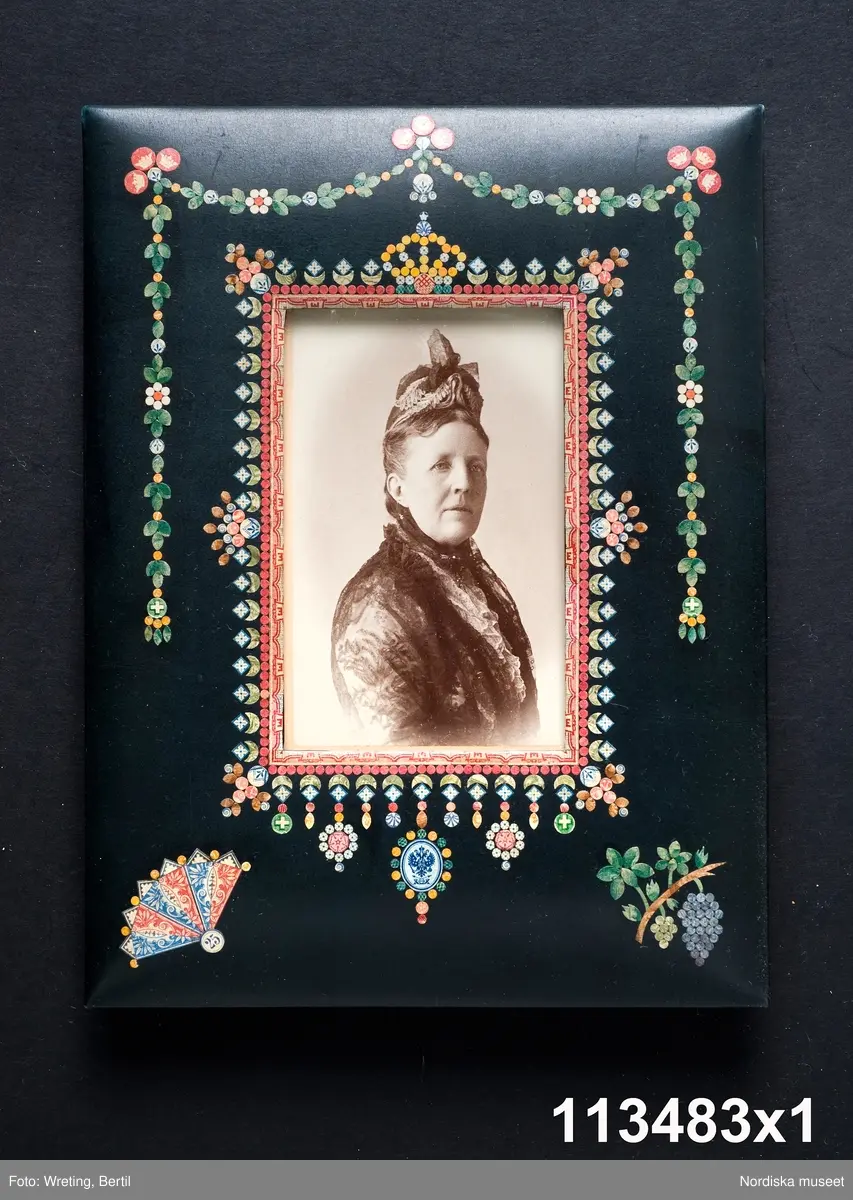 Huvudliggaren:
"a-å
Skrivbordsuppsats, 25 olika pjäser, däribland lampa, ljusstake m.m. allt ornerat med frimärksklipp. Jämte 4 mindre lådor med lösa frimärksdelar. Gåva 17/5 1909 av fru Augusta Cronholm f. Bratt, Birgerjarlsgatan 18, Stockholm."