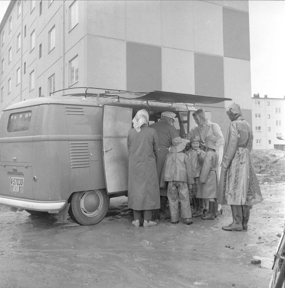 Bøler, Oslo, 18.10.1958. Boligblokker og mennesker i regntøy samlet rundt folkevognbuss.