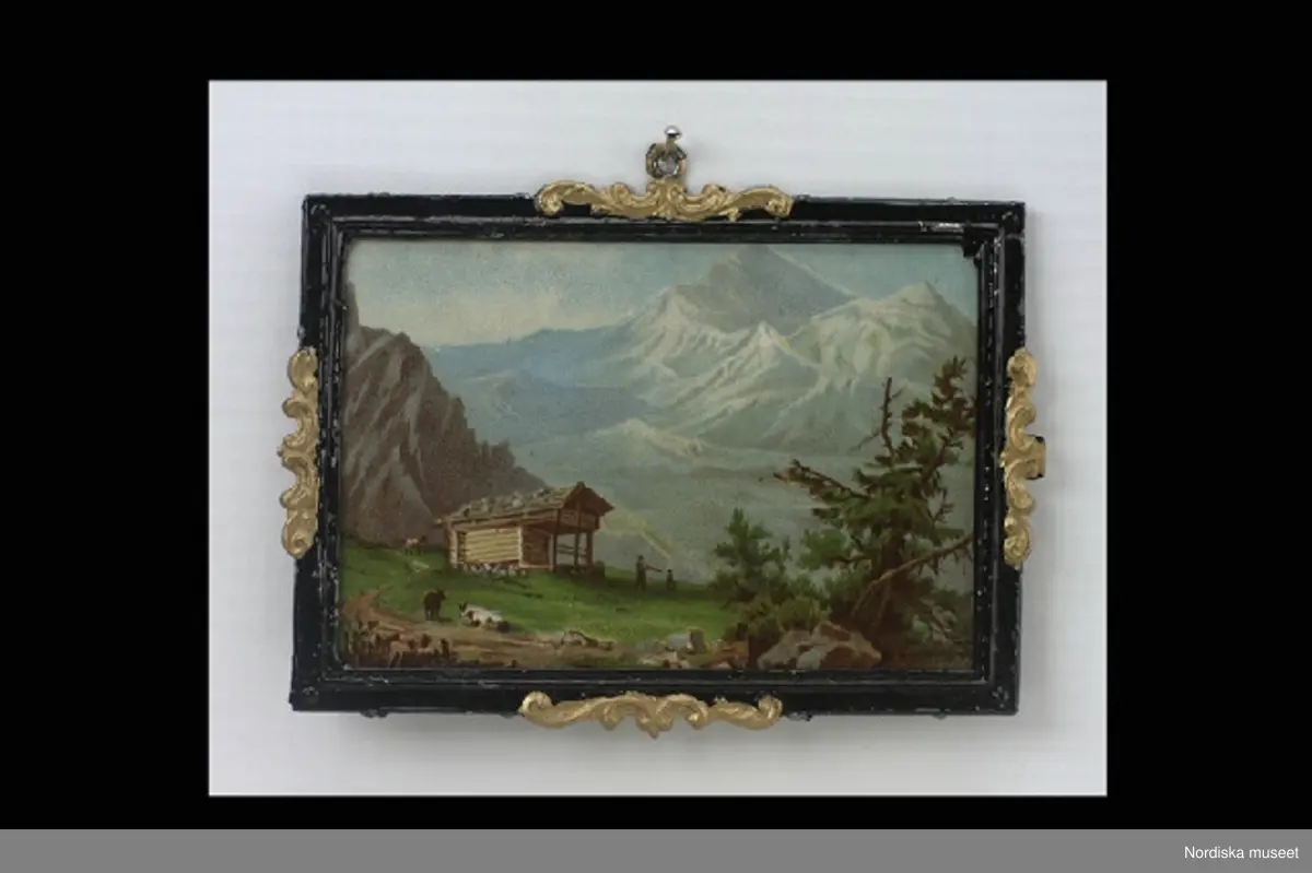 Inventering Sesam 1996-1999:
L 8,7 cm
B 6,3 cm
3 st dockskåpstavlor, flerfärgstryck på papp, tunn ram av tenn, svartmålad med guldmålade ornament.
a) Motiv; alplandskap med litet hus.
b) Motiv; by i alplandskap med kyrka, text i nedre högra hörnet "St Maurice".
c) Motiv; borg på bergssluttning, text i nedre högra hörnet "Rheinstein".
Tillhör dockskåp inv 164.570. Brukad av givarinnan född 1886.
Leif Wallin nov 1997