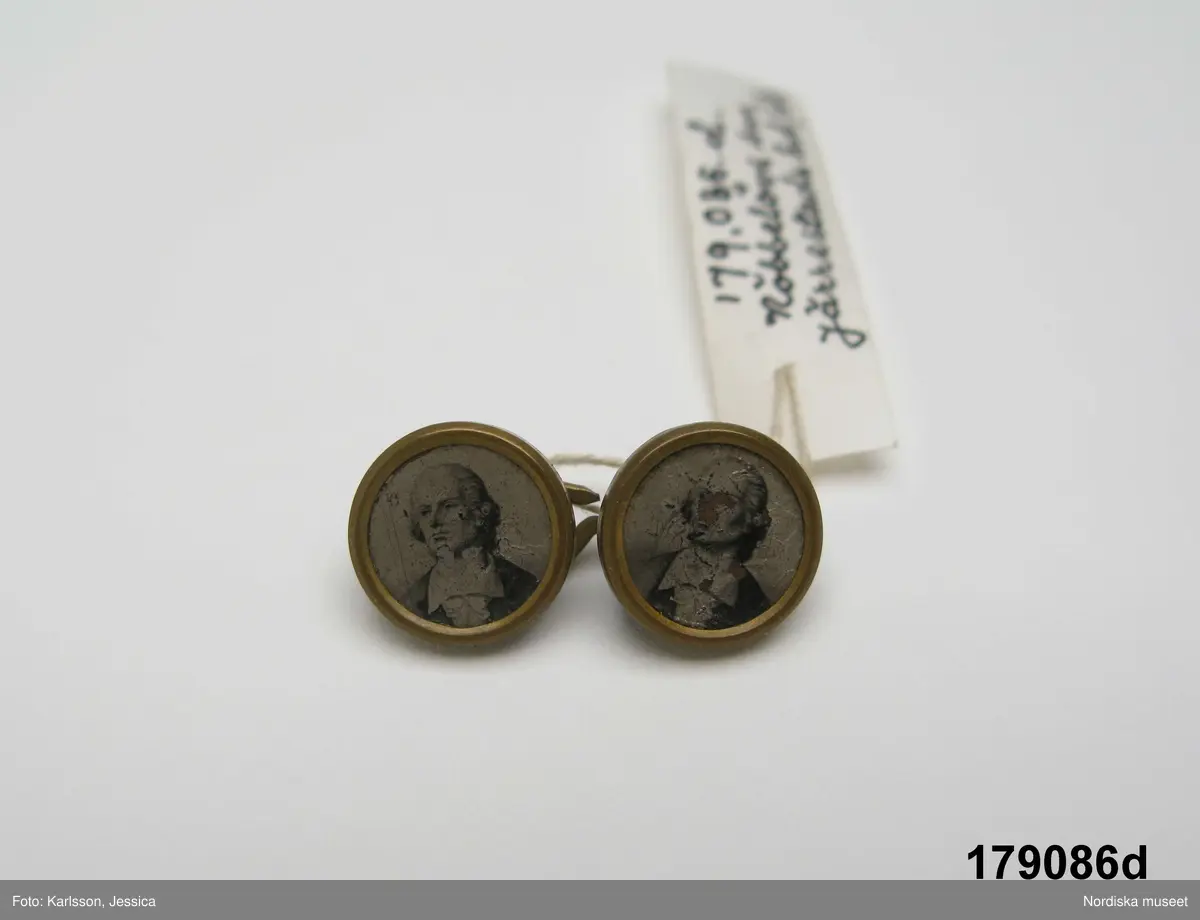 Huvudliggaren (år 1929):
"179086 a-d. Manchetter fr. Gislövs by, Nöbbelövs sn, Järrestads hd, Sk.  1 par, av vitt linne m. hålsöm o spete i kanten, dubbla m. länkknappar av mässing m. infällga porträtt. I [från] Fru Hanna Jönsson, Borrby."

Bilaga:
Förteckning


Katalogkort:
Finns ej.

a-b: Manschetter. Längd: ca 20 cm. Bredd: 12,5 cm. Spets: 1 cm. Teknik: Tuskaft. Enkel utdragssöm. Maskintillverkning - spets. Handsömnad.
a-b: Ett mar manschetter av tuskaftat vitt bomullstyg. Dubbelvikt tygstycke, längd: 20 cm, bredd: 7,5 cm, med fastsydd manschettkant med rundade hörn, längd: 16,5, bredd: 5 cm inkl spets. Manschetten har broderad kantbård i yttre kant, ca 1 cm bred, maskintillverkad spets runt framkanter. Två sydda knapphål i armstycket.
/Inga-Lill Eliasson 2009-03-19
