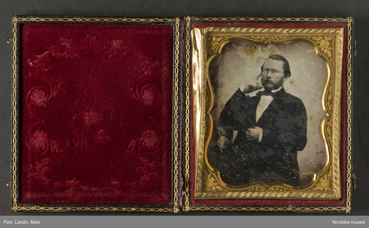 Porträtt av okänd man. Sittande, iklädd svart jacka, vit skjorta och svart halsduk. Glasögon och skägg. Dagerrotyp / daguerreotyp i sidenfodrat etui av amerikansk typ, ca 1850. Nordiska museet inv.nr 230443.
-
Portrait of an unidentified man, c. 1850. Sixth-plate daguerreotype in velvet lined case with gilt decorations.