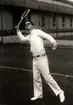 Nordiska Kompaniet visar tenniskläder oktober 1928. Ung man iförd tenniskläder och solglasögon svingar en tennisracket, i andra handen håller han en boll.