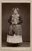 Porträtt av stående kvinna iklädd folkdräkt. På kortet är noterat att hon bär bruddräkt från Ingelstads härad i Skåne. Nordiska museet inv.nr. 18541C