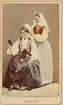 Dräktdockor med huvuden skulpterade av C A Söderman, visade på världsutställningen i Paris 1867. Två kvinnor i folkdräkter från Blekinge, varav en hjälper den andra med huvudbonaden. Handkolorerad version.