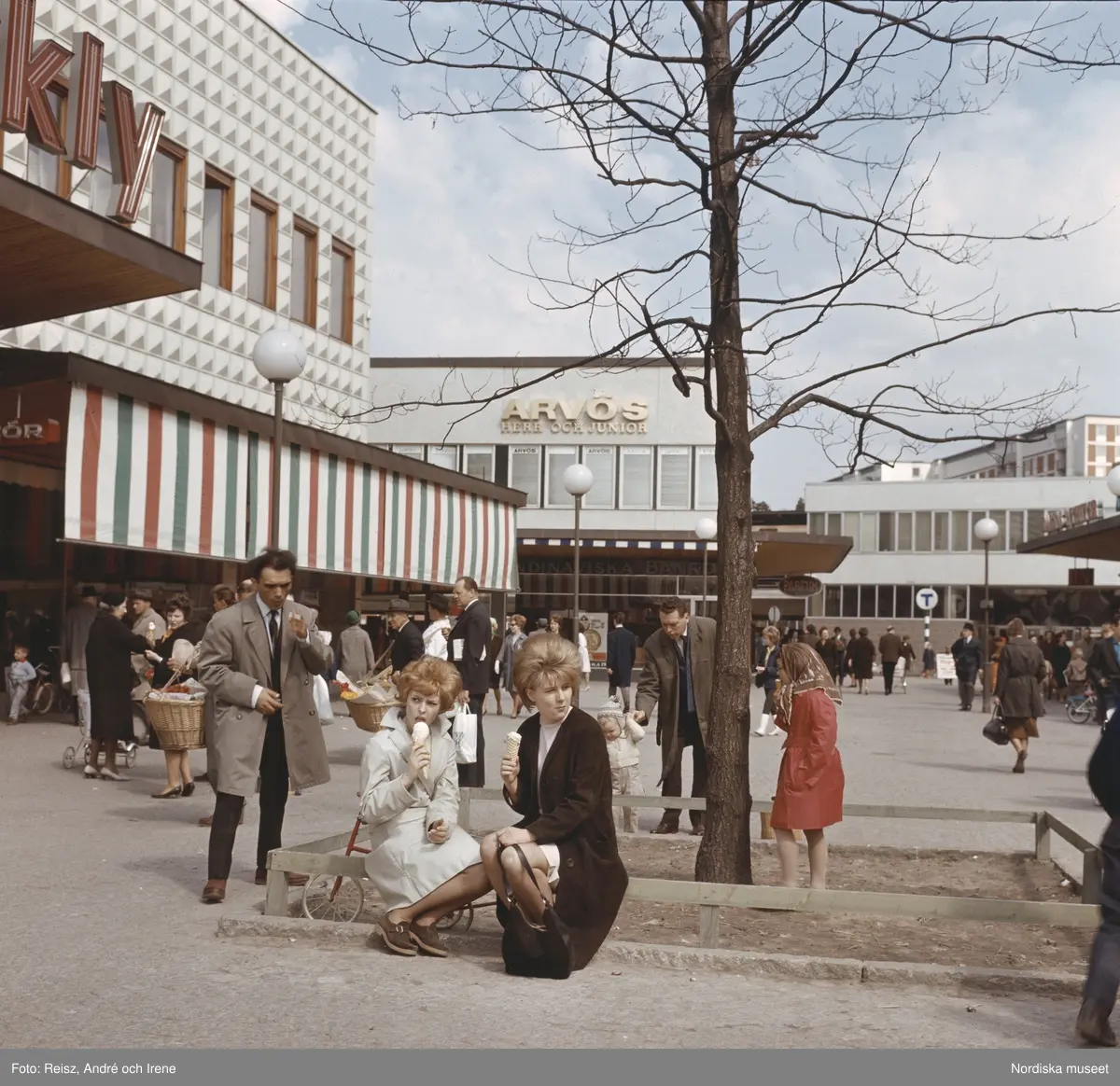Förort, Farsta centrum. Folkliv runt torget, två kvinnor äter glass under ett träd.