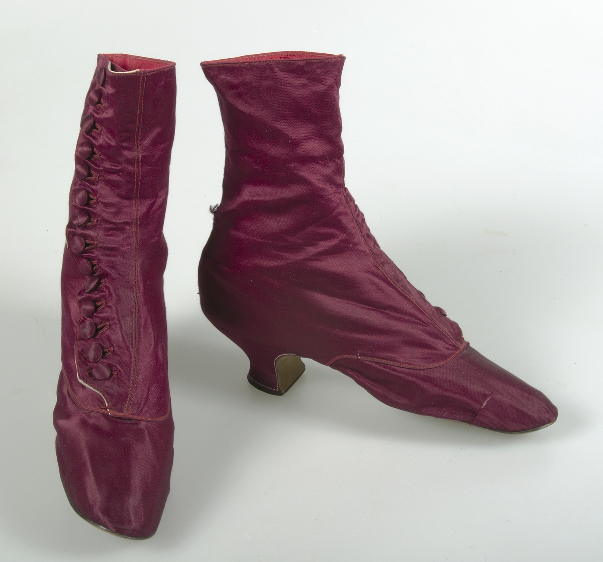 Kängor av vinrött siden. Knäppt med 14 klädda knappar. Brun lädersula. Fodrade med vit lärft, vitt skinn och rött siden.