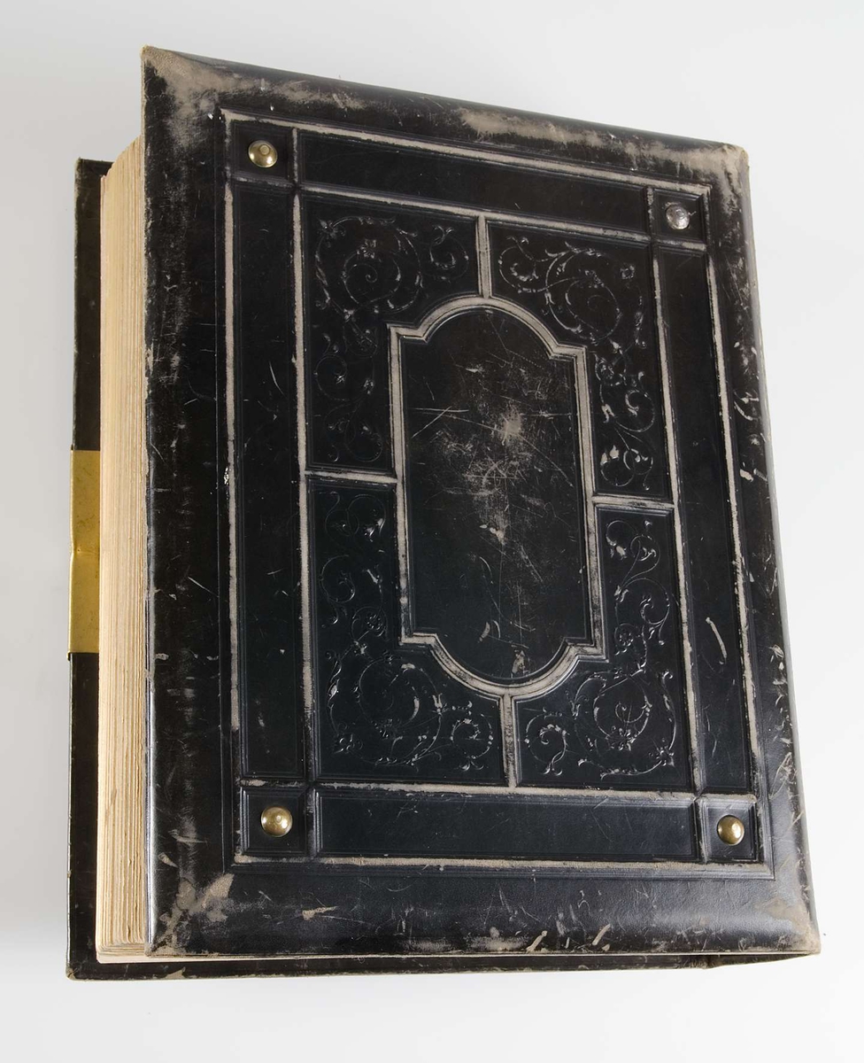 Fotoalbum med pärmar av svart läder och dekor i relief och guldtryck. På framsidans pärm finns en mittspegel av glas på vilket ett landskapsmotiv i månsken är målat. På baksidans pärm finns fyra nitar av metall.
