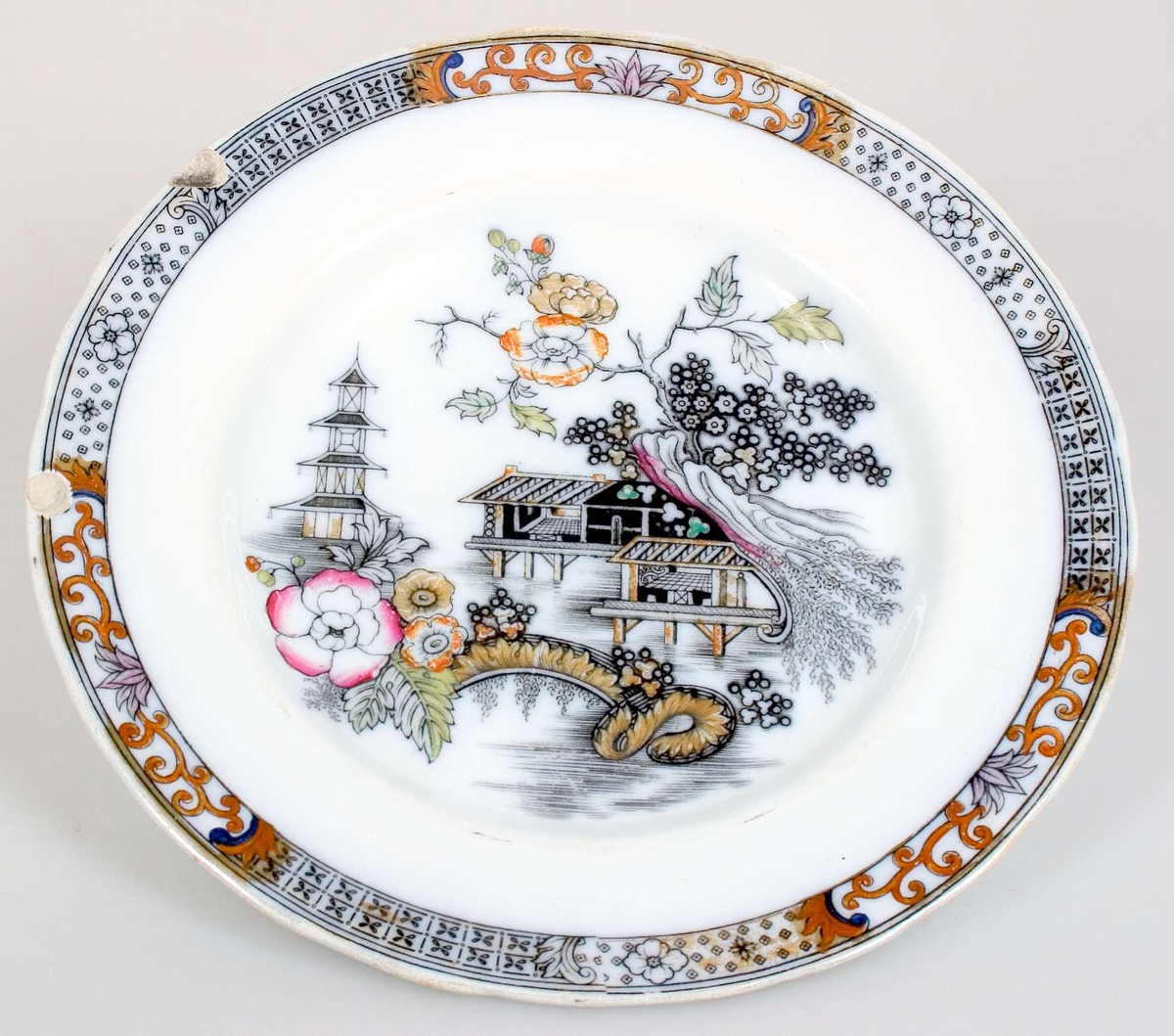 Flat tallrik, vit glaserad med kolorerad svart gravyrdekor i guld, rött, orange, grönt, brunt och ljuslila. tryckt svart stämpel: Japan Ironstone China RÖRSTRAND.