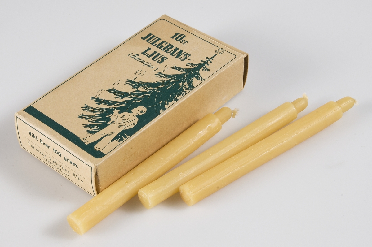 Två kartonger av brunbeige papp med grönt tryck, bild av julgran och ett barn och text: 10 st JULGRANSLJUS, (Barnljus), Tekniska Fabriken Elky, Stockholm. Innehåller 10 gulvita stearinljus. 