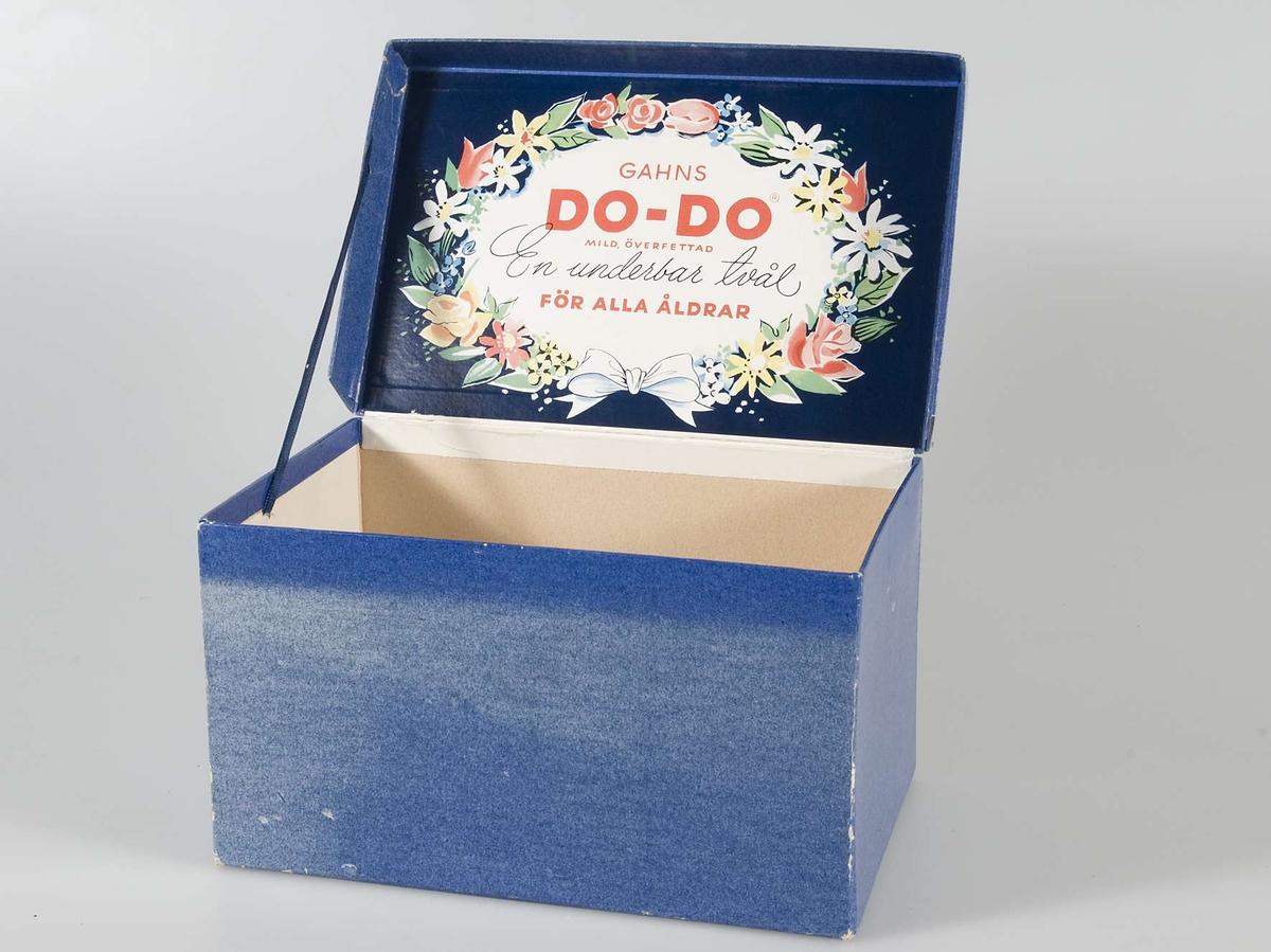 Kartong av papp för tvålar. Klädd med blankt blått papper. Locket fäst baktill. På lockets ovansida och insida en bild av en blomsterkrans. Inuti denna text i rött: " Gahns DO-DO mild överfettad......"  På kartongens insida är fäst ett blått band av syntetmaterial. Dess andra ände har varit fäst vid lockets sidokant. Pappret trasigt på lockets insida.