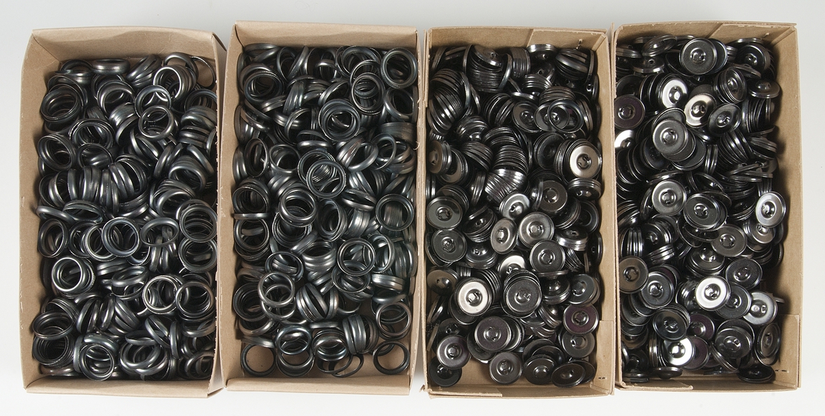 Originalförpackning, kartong av oblekt papp indelad i tre fack med 100 knappformar i tre delar, dels av svart metall, ringar och knappar med kanal, dels runda ljusbruna pappskivor. Knappformarnas diameter ca 2 cm. Ovanpå locket papperstejp, på sidan etikett med text: HAGEX H & S knappformar DUBBELMONTAGE (utan inlägg) 5 gross 36" svart Art. 2 (med kanal).
