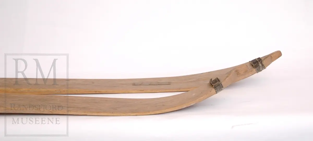 1 par ski, hoppski. Hickory, korkenebb spiss, lyse brune. Tre renner. Tjærebånd på tuppene. Påskrudd metalltåbinding og feste for Kandahar fjærbinding (mangler). Sprukne, reparert med metallplate