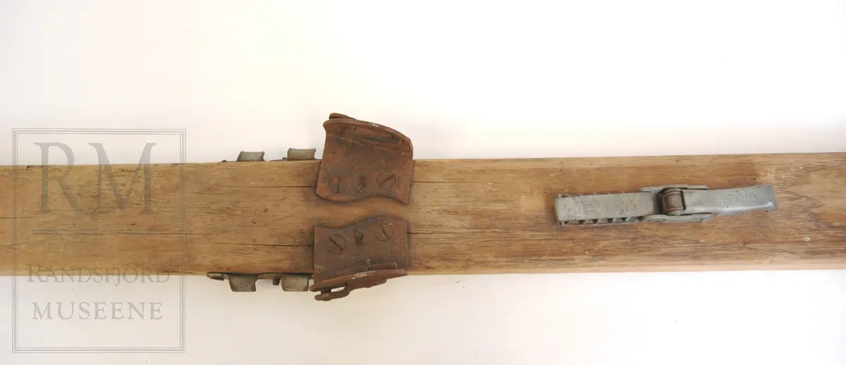 1 par ski, hoppski. Hickory, korkenebb spiss, lyse brune. Tre renner. Tjærebånd på tuppene. Påskrudd metalltåbinding og feste for Kandahar fjærbinding (mangler). Sprukne, reparert med metallplate