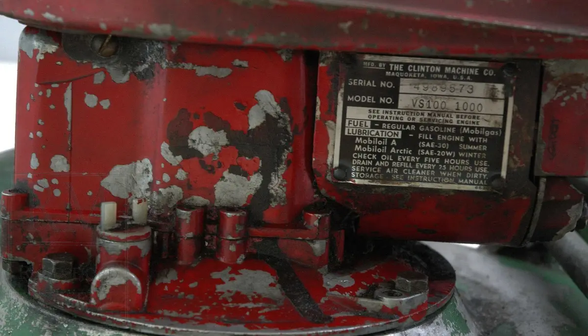 Gressklipper i aluminium med 4 gummihjul. Motor midt på. Motor har boks festet på siden. Metallhåndtak. Gresset blåses ut til høyre.