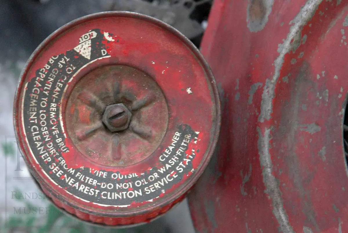 Gressklipper i aluminium med 4 gummihjul. Motor midt på. Motor har boks festet på siden. Metallhåndtak. Gresset blåses ut til høyre.