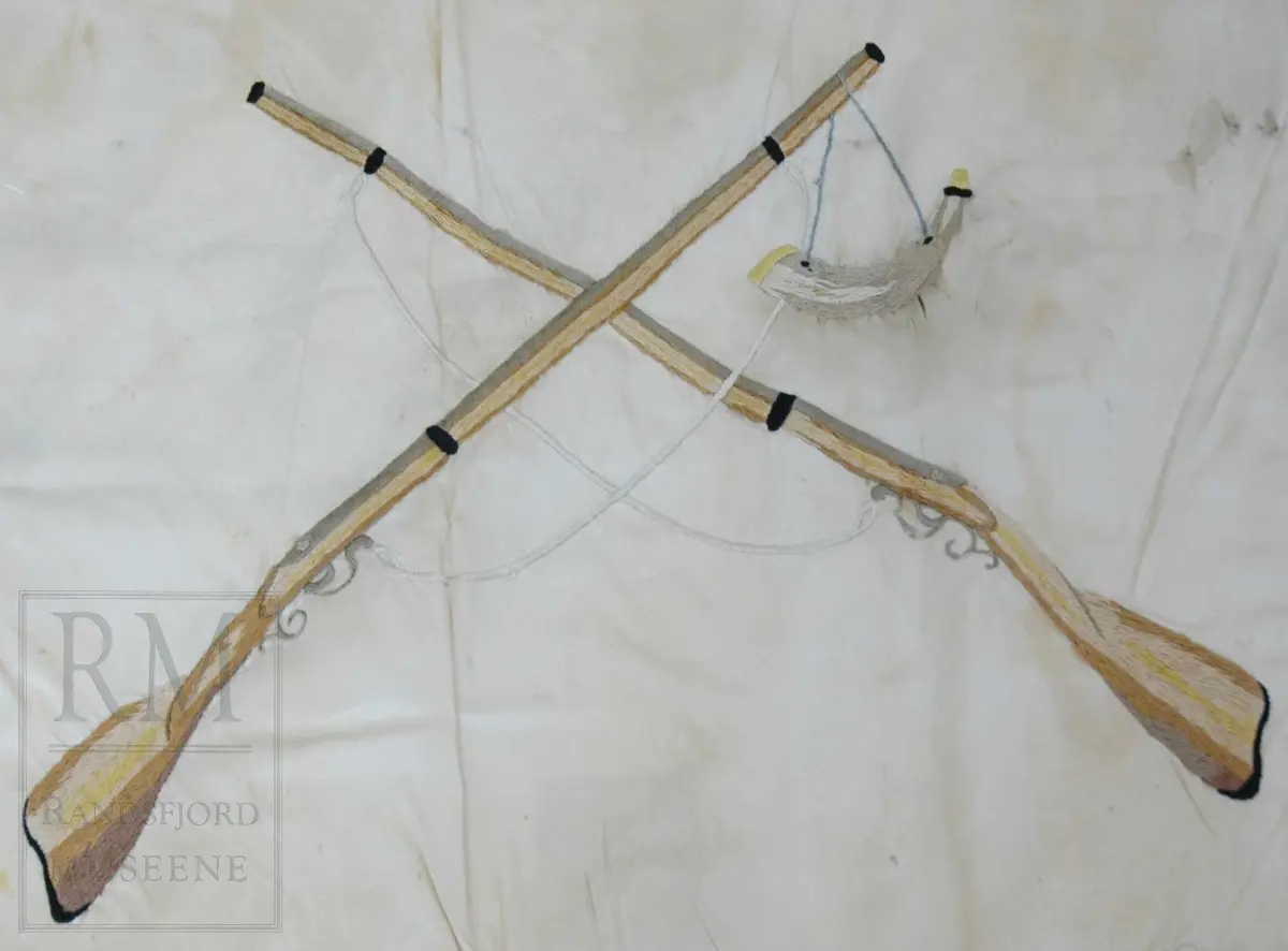 Fane av hvit silke. Løpegang på den ene siden har revnet. Brodert tekst, samt eikebladskrans med sløyfe omkring to gevær med påhengende krutthorn.