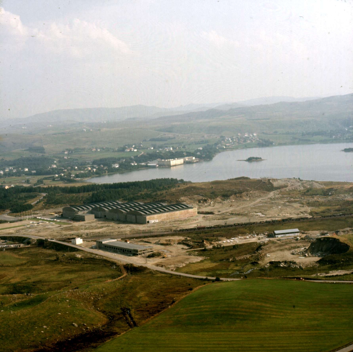 Kverneland fabrikk, produksjonen og fabrikken: flyfoto av fabrikken på Øksnevad, teke frå nordvest, fabrikkanlegget på Kvernaland og Frøylandsvatnet i bakgrunnen 24. juni 1969.