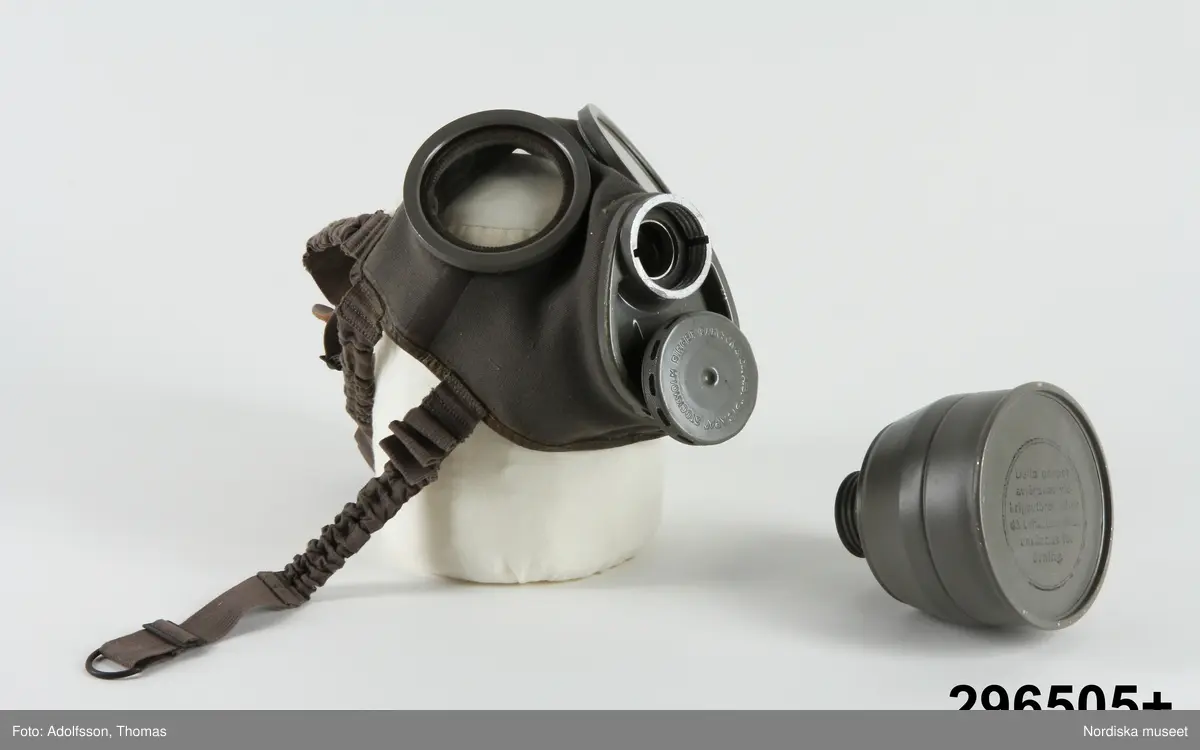 Huvudliggare:
"GASMASK, tyg, metall; förvaras i fodral av hårdpressad papp; se bilaga. Mått fodral Br 19 cm, Tj 12,5 cm, H 25,8 cm.
G från museets skyddsrum, 1939. /1973/ 8/8 Nordiska museet, Stockholm."

Bilaga [kopia av katalogkort]:
"Skyddsmask, storlek 3, i två delar. Ansiktsskydd av kraftigt grått tyg med fastsättningsband av tyg och resår. Skinnskodd kant.
Två syngluggar (diam 8,5 cm) med metallkant och glas. På insidan imskydd av celluloid, fäst med en avtagbar metallfjäder. Imskydden är utbytbara.
Framför näsa och mun ett äggformat metallstycke med två gängade hål. I 'munhålet' sitter ett runt metallstycke (diam 6 cm, h 1 cm) med hål längs ytterkanten. I munstycket sitter ett gummimembran, som ger efter vid utandning. Runt den plana sidans kant står inpressat 'STOCKHOLM BIRGER CARLSON & Co. A.B. 'BICAPA' '. Läderpackning avslutar det gängade partiet. I inandningshålet ligger en gummipackning. Här ska en grå metallbehållare fastskruvas, vilken i sin yttre del är försedd med ett skyddspapper på vilket står: 'Detta papper avlägsnas vid krigsutbrott eller då behållaren ska användas för övning'.  Den gängade delen är skyddad av en kapsyl. På behållaren är stämplat ''1939' B13341E' samt tre kronor. På ena sidan sitter ett blått varu-märke. I fodralet finns också en förpackning stämplat av samme tillv och med årtalet 1939. På förp står 'Imskivor / skyddas för fukt. Får ej avtorkas. Vidröras endast i kanten.' Alltsammans ligger i en grå oval kartong av hårdpressad kartong. På locket är tillverkarens namn inpressat och strax nedanför locket står på ena sidan på en silverfärgad etikett 'FÖR AKTIVT LUFTSKYDD / SVENSK TILLVERKNING'. Runt kartongen (fodralet) sitter tygband, så att skyddsmasken kan bäras över axeln.
1973-08-08 Fynd i Nordiska museet
1976-02-27 BR"