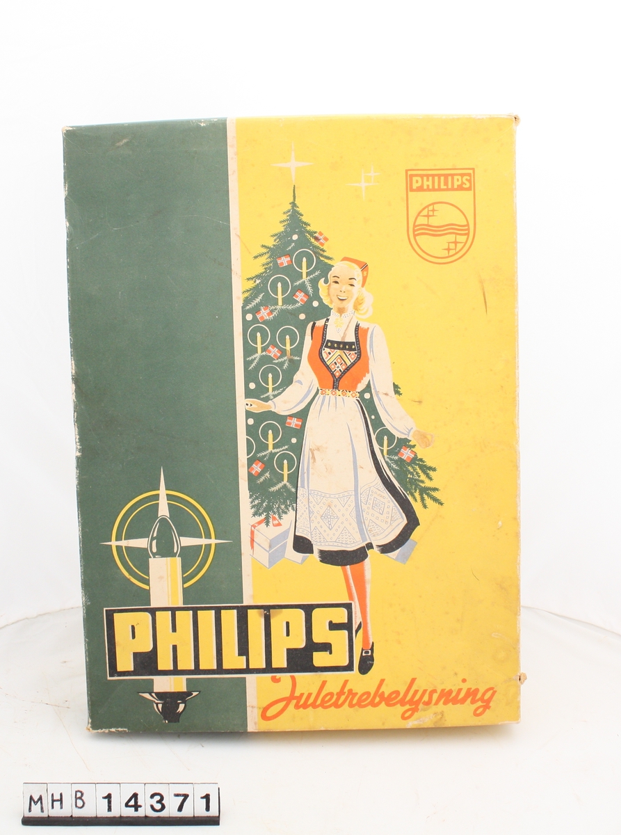 Rektangulær eske med lokk til juletrebelysning. På lokket er en bunadskledd jente foran et pyntet juletre med gaver under.Esken inneholder pappemballasje for juletrelys, samt en til og fra lapp festet til en snor.