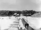 Hägernäs flygstation, vintertid 1925. Vy från bryggan. Tälthanger och hus i bakgrunden. Två personer på bryggan i förgrunden.