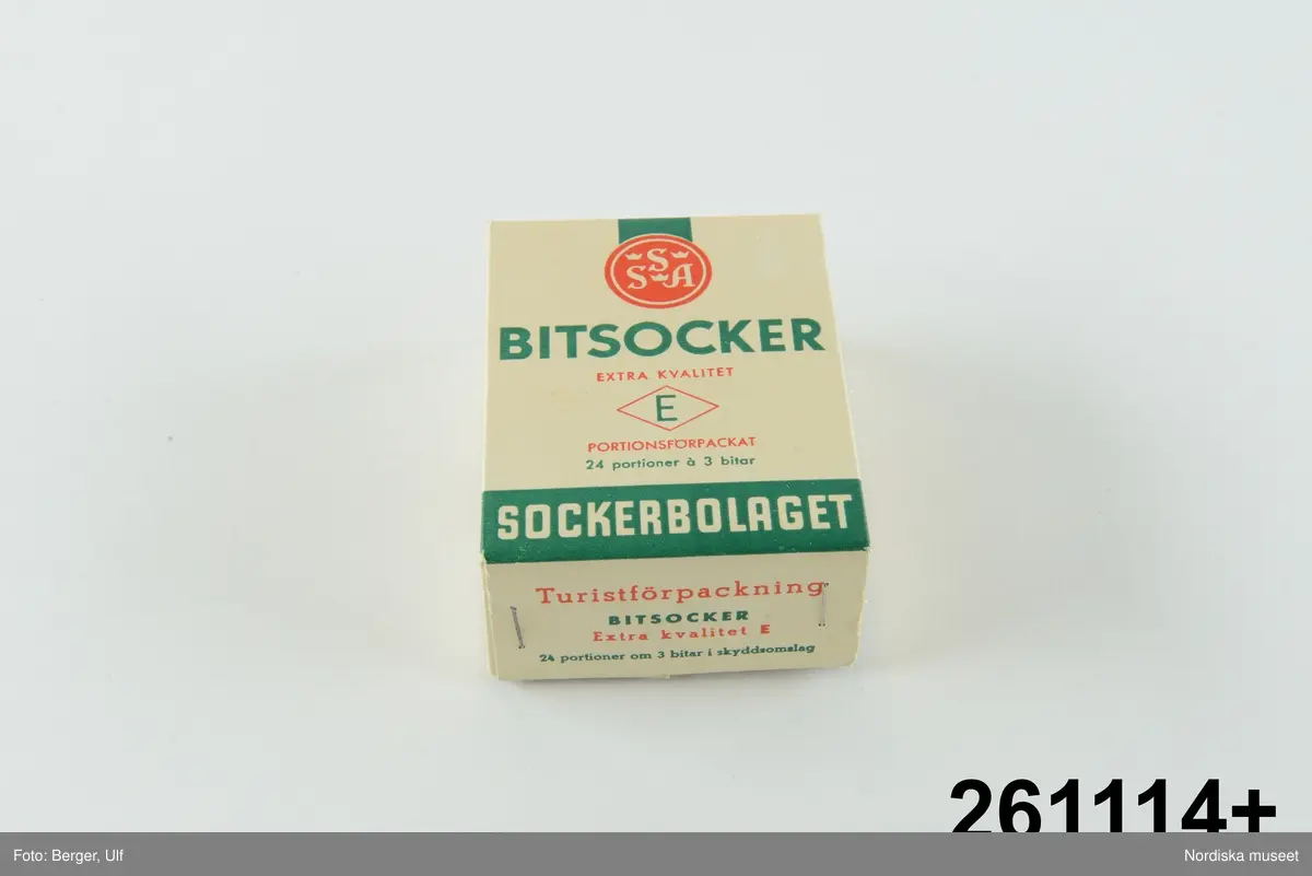 Huvudliggaren år 1960: 
”Ask, av kartong, överfalsat lock, alla hörn med häftade flikar; för ’Bitsocker extra kvalitet E portionsförpackat, 24 portioner á 3 bitar. Turistförpackning. Svenska Sockerfabriks AB.’ L 9,8 cm, Br 7,4 cm, Tj 3,8 cm. Gåva den 30/8 1960 av Fru Elsa Lindberg, Stockholm.”