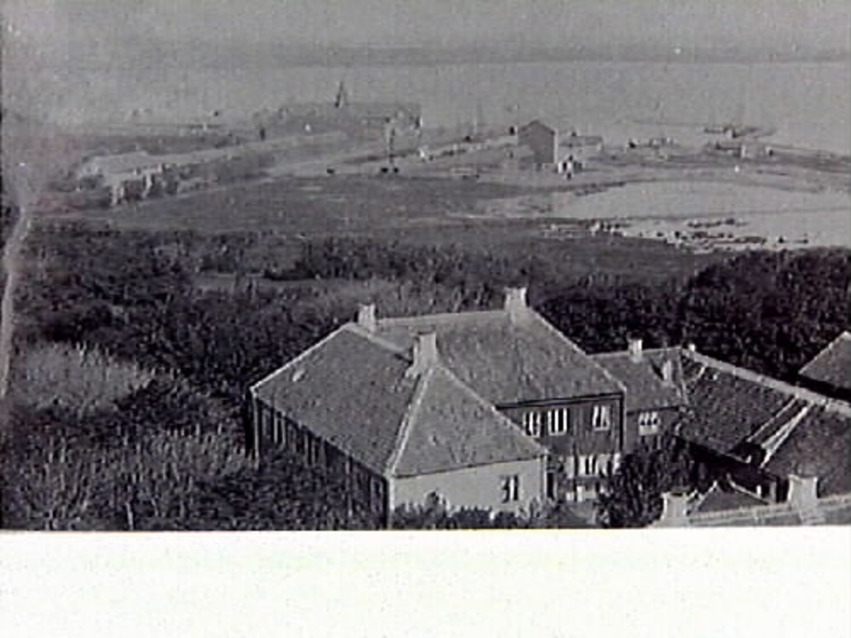 Foto taget mellan åren 1866-1874, fotografen förmodas vara Birger Sjöberg. I förgrunden gården i hörnet Västra Vallgatan-Kyrkogatan, nuvarande kv Prosten. Här bodde och verkade snickarmästare Johan Salomon Tingström (1835-1911). Han kom till Varberg 1864 och var en oerhört skicklig möbelsnickare med verkstad inne på gården. Efter en brand på gården sensommaren 1889 lät han uppföra det stenhus som står där idag. I bakgrunden syns hamnen med bl a de båda badhusen. När järnvägen anlades skedde det på utfyllnad av viken.