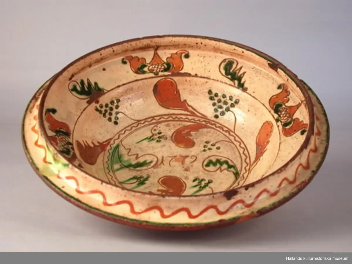 Fat av lergods, insidan täckt med vitlera med ristad dekor och grön glasyr. Märkt 1779.