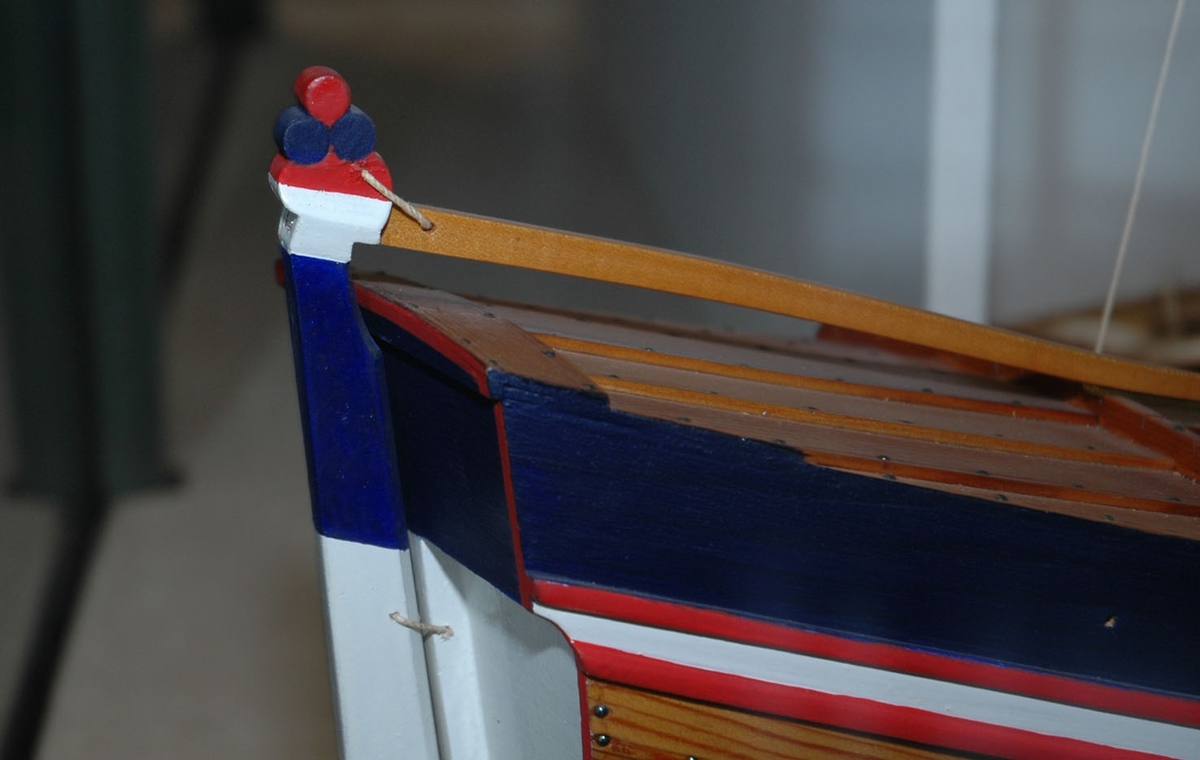 Klinkbygget  modell med løfting og ror, rorkult, 4 årer (NSM.07948-51), mast, tiljer,2 tofter. Rigget med seil. Lakket skrog, øverste bordgang malt hvit med to smalere røde linjer på hver side. Løfting blå sider. Akterspeil hvitt. Ror over vannlinjen hvitt og blått.  Målestokk 1:18.