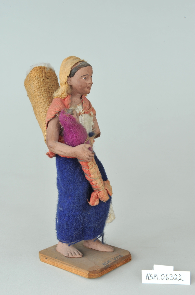 Viser kvinne med barn på armen og kurv på ryggen. Venstre arm mangler fra albuen og ned.