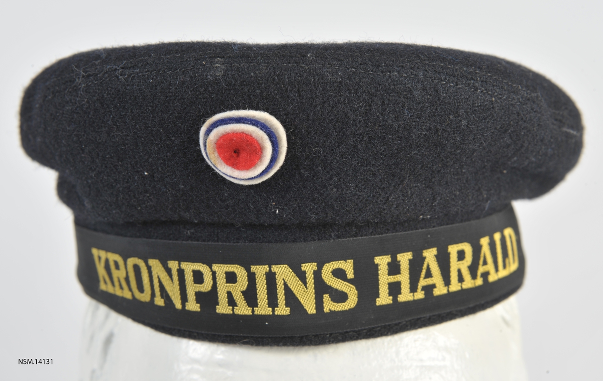 Rund matroslue i vadmel med navnet Kronprins Harald rundt bremmen.