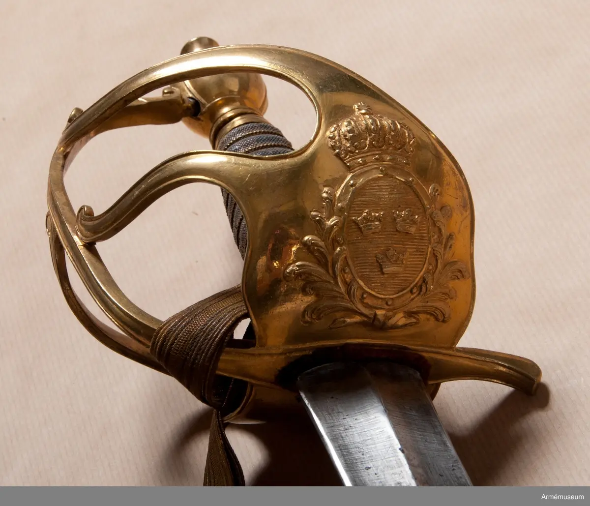Fäste av förgylld mässing med två yttre och en inre sidobygel. Parerplåten har en krönt sköld omgiven av stiliserade palmkvistar. Kaveln klädd med hajskinn och lindad med en tvinnad,  förgylld mässingtråd. 

Klingan är rak och tveeggad. Bredd vid fästet: 37 mm. Upptill rester av blånering och dekorerad med tre kronor, omslutna av två palmkvistar.