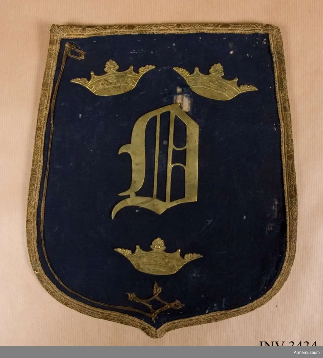 Monogram Oscar I.
Mått: 265 x 220 mm.
Framsidan är täckt  med ett ganska tunt ylletyg, vävt i kypert. Locket är kantat  med ett band i guldgalon. Innanför bandet är som dekoration fastsytt ett mycket smalt guldband, som endast är kvar på ena  sidan och upptill och vid den andra sidan är helt borta. På  mitten av locket är ett 90 mm högt monogram för Oscar I, däröver två öppna kronor och under monogrammet en Öppen krona. Locket är fodrat med ett ljusgult bomullsfoder vävt i tuskaft. Färgen skall väl vara saffianliknande (= marokäng eller saffian, mjukt läder av get eller bockskinn). En ficka finnes på mitten av fodersidan och sträcker sig tvärs  över från sida till sida och går på djupet till lockets nedersta kant. Över ficköppningen fälles ett lock, kantat med  guldband och upptill fastsatt under den guldgalon som går runt  lockets kant. Vilket regemente som haft detta lock med detta utseende vet jag  just nu inte, men gissar på, som hade mörkblå sabeltaska med gul saffian tiden 1814-54. Kanske är det teaterrekvisita? Åke Dalbeck tror "barnleksak" f kungl. barn.