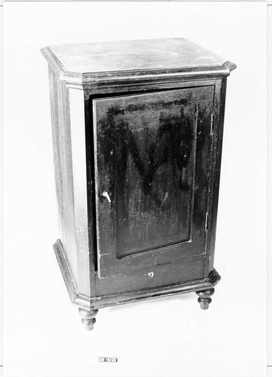 Platen (lokket) er hengslet i bakkant. Dør med vrider i messing. Topplate med hull til vaskevannsfat. Topplaten er marmorert. Skuff i underkant.