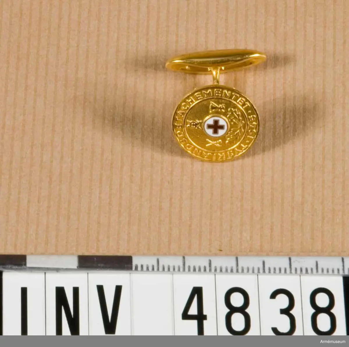Förgyllda med ett litet rött kors på vit emalj i mitten, runt detta ett fält med två eklövskvistar, armétecken samt runt  kanten texten Tysklands datachement. Samhörande ett par manschettknappar fastsatta i svart bottenplatta med kudde av  vit flanell.
