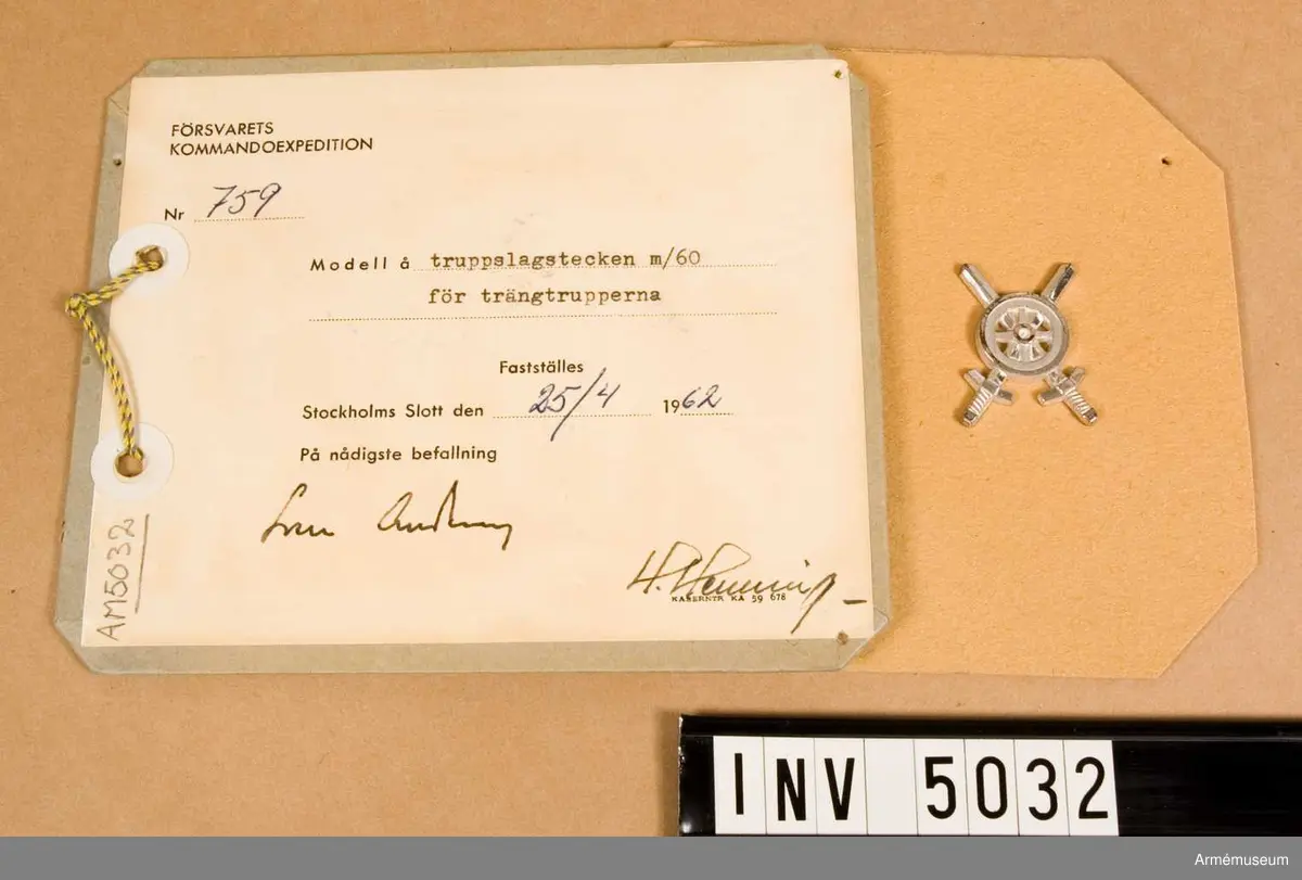 Tillverkat av metall. I likhet med emblemen till  trängtruppernas äldre uniformer är det här utfört i silverfärg. Samma motiv som i 1939 års modell, ett kärrhjul på två korslagda svärd, men något annorlunda utformat.
