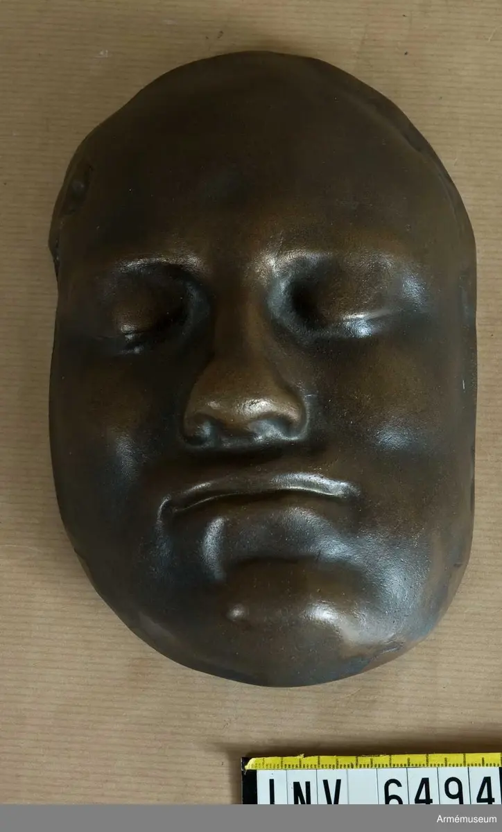 Bronsmask föreställande den döde Karl XII.

Enl styresman Olle Cederlöfs anteckningar med anledning av gåva AM.066063 (AM 73/475) är detta inte en dödsmask. 

"Proportionerna i ansiktet stämmer inte med kraniets proportioner enl 1918 års gravöppning - utan en av den schweiziske medaljgravören Hedlinger gjord frihandsmodellering inför konungens lik på Karlberg 1718. Hedlingers modell nu endast avsedd att ligga till grund för hans uppdrag: Att modellera en reliefbild för konungens mynt och minnespenningar. Hedlinger anlände till Sverige 1718-. Konungen hade då avlidit och Hedlinger hade aldrig sett Karl XII i levande livet, han tog chansen att fånga konungens ansikte inför 'lit de parade' på Karlberg. Hedlingers 'dödsmask' har senare avgjutits i gips, brons och  järn i olika sammanhang."