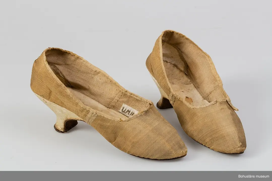 Ur handskrivna katalogen 1957-1958:
Fruntimmersskor
Sulornas L. c:a 23 cm. Chagrinerat siden, gult. Sulor av läder, innersulor o klack; av vitt skinn. Tyget nt trasigt. Troligen fr 1700-talet. Bohuslän

Antecknat i Gåvobok 1875, december: Fru Gottfrida Wesslau. Ett par skor från förra århundradet.