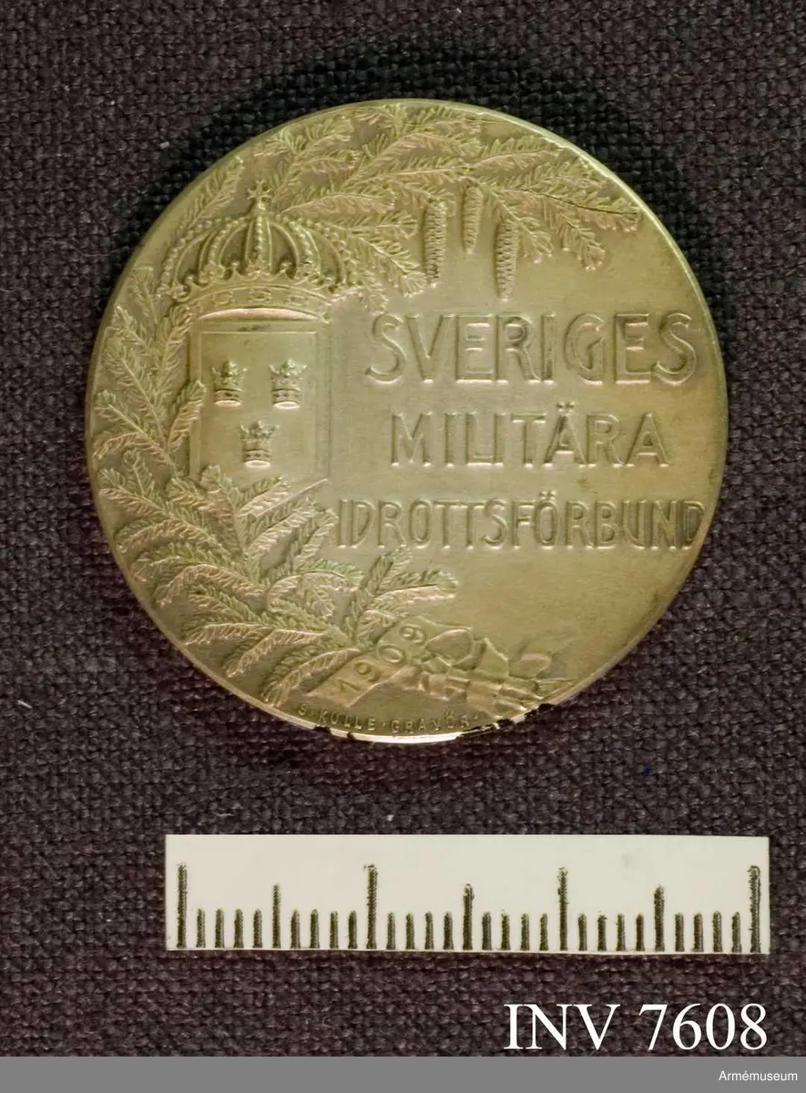 I relief på framsidan (adversen) en grankvist, riksvapnet och texten Sveriges Militära Idrottsförbund och årtalet 1909. På frånsidan (reversen) idrottens beskyddarinna med riksvapnet i relief, tillverkar- och årtalsstämplar. Frånsidan saknar text.

Erövrat av fanjunkare Sigfrid H Hultquist 1912 (sic). Förvaras i gul rund ask med blått lock tillsammans med AM 7607.
