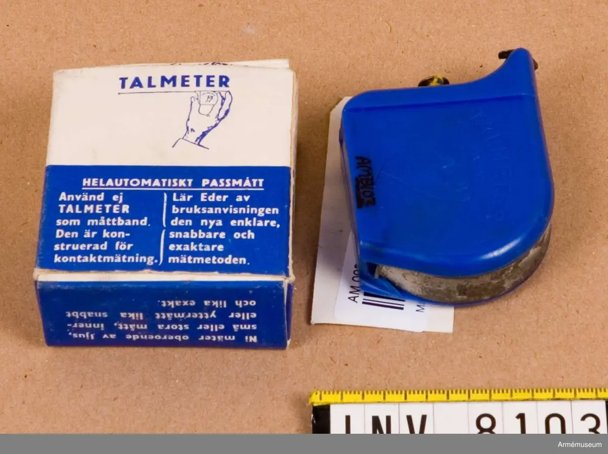 Tillverkad av blå plast och måttbandet av stål. Kåpan är märkt  med "Talmeter patent" och på motstående sida "T. A. LJUNGBERG SWEDEN". Bandets längd är 2 m. Bruksanvisning finns i  förpackningen.Ingår i fotomaterielsats 7 låda 1. 