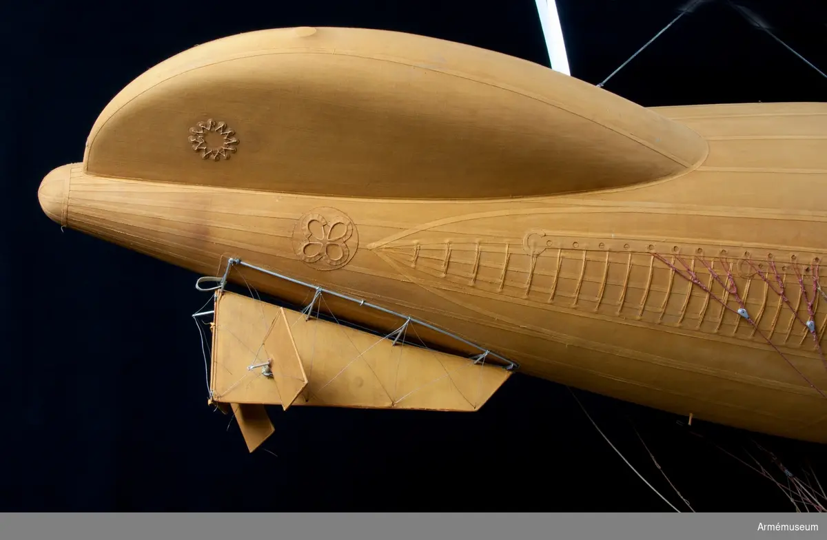 Modell av modifierad spaningsballong från ca 1928. Stora likheter med den schweiziska motoriserade M-typen av Fesselballon från samma år. Formen är långsträckt, spolformig och överklädd med gult bomullstyg av en tät kvalitet (gummiväv). Det är svårt att avgöra stommens material men det kan vara aluminium då det användes till att bygga stomme av till de "riktiga" luftskeppen. Modellen är mycket tung och därför kan det även tänkas att stommen är tillverkad av exempelvis gips. Ballongen hänger i en kraftig stålwire. Under ballongen hänger gondolen. Denna har en stomme av metall och ståltråd och är överklädd med silverfärgad väv, samt har två pontoner som "landningsställ". På ömse sidor hänger en väska. I aktern finns en propeller och på ena sidan samt mitt fram finns en ratt. Under spaningsballongens mittlinje hänger rader av linor - mitten 1 st, styrbord 4 st och babord 8 st). Dessa är mycket konstfullt utförda med s k knävringar, (styrbord 7 st, babord 10 st) fastsplitsade i ändorna. Flera linor har små öglor infästade längs med linan. Linorna är upphängda i block, - styrbord och babord har 20 st vardera. Under ballongens akter sitter balansrodret fästat varav ett roder är fast och tre är rörliga.

Se vidare Nordisk Familjebok 1912, sidan 1310, rubriken "luftskepp".