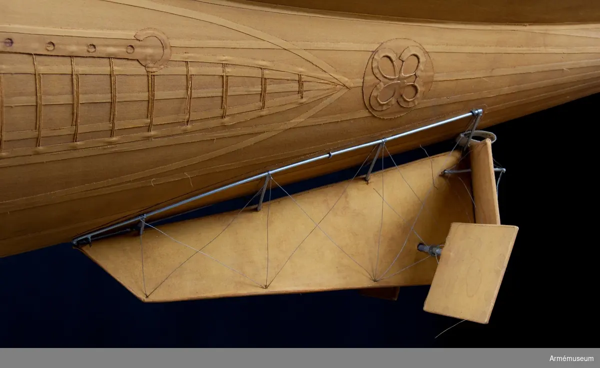 Modell av modifierad spaningsballong från ca 1928. Stora likheter med den schweiziska motoriserade M-typen av Fesselballon från samma år. Formen är långsträckt, spolformig och överklädd med gult bomullstyg av en tät kvalitet (gummiväv). Det är svårt att avgöra stommens material men det kan vara aluminium då det användes till att bygga stomme av till de "riktiga" luftskeppen. Modellen är mycket tung och därför kan det även tänkas att stommen är tillverkad av exempelvis gips. Ballongen hänger i en kraftig stålwire. Under ballongen hänger gondolen. Denna har en stomme av metall och ståltråd och är överklädd med silverfärgad väv, samt har två pontoner som "landningsställ". På ömse sidor hänger en väska. I aktern finns en propeller och på ena sidan samt mitt fram finns en ratt. Under spaningsballongens mittlinje hänger rader av linor - mitten 1 st, styrbord 4 st och babord 8 st). Dessa är mycket konstfullt utförda med s k knävringar, (styrbord 7 st, babord 10 st) fastsplitsade i ändorna. Flera linor har små öglor infästade längs med linan. Linorna är upphängda i block, - styrbord och babord har 20 st vardera. Under ballongens akter sitter balansrodret fästat varav ett roder är fast och tre är rörliga.

Se vidare Nordisk Familjebok 1912, sidan 1310, rubriken "luftskepp".