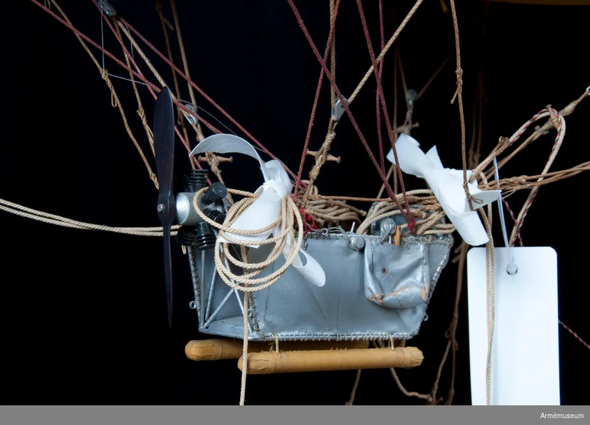 Modell av modifierad spaningsballong från ca 1928. Stora likheter med den schweiziska motoriserade M-typen av Fesselballon från samma år. Formen är långsträckt, spolformig och överklädd med gult bomullstyg av en tät kvalitet (gummiväv). Det är svårt att avgöra stommens material men det kan vara aluminium då det användes till att bygga stomme av till de "riktiga" luftskeppen. Modellen är mycket tung och därför kan det även tänkas att stommen är tillverkad av exempelvis gips. Ballongen hänger i en kraftig stålwire. Under ballongen hänger gondolen. Denna har en stomme av metall och ståltråd och är överklädd med silverfärgad väv, samt har två pontoner som "landningsställ". På ömse sidor hänger en väska. I aktern finns en propeller och på ena sidan samt mitt fram finns en ratt. Under spaningsballongens mittlinje hänger rader av linor - mitten 1 st, styrbord 4 st och babord 8 st). Dessa är mycket konstfullt utförda med s k knävringar, (styrbord 7 st, babord 10 st) fastsplitsade i ändorna. Flera linor har små öglor infästade längs med linan. Linorna är upphängda i block, - styrbord och babord har 20 st vardera. Under ballongens akter sitter balansrodret fästat varav ett roder är fast och tre är rörliga.

Se vidare Nordisk Familjebok 1912, sidan 1310, rubriken "luftskepp".